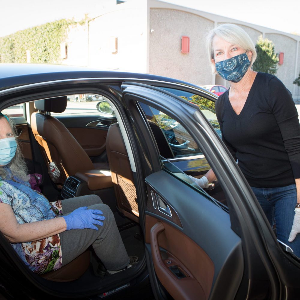 Volunteer driver wearing mask helps rider who is wearing mask out of car